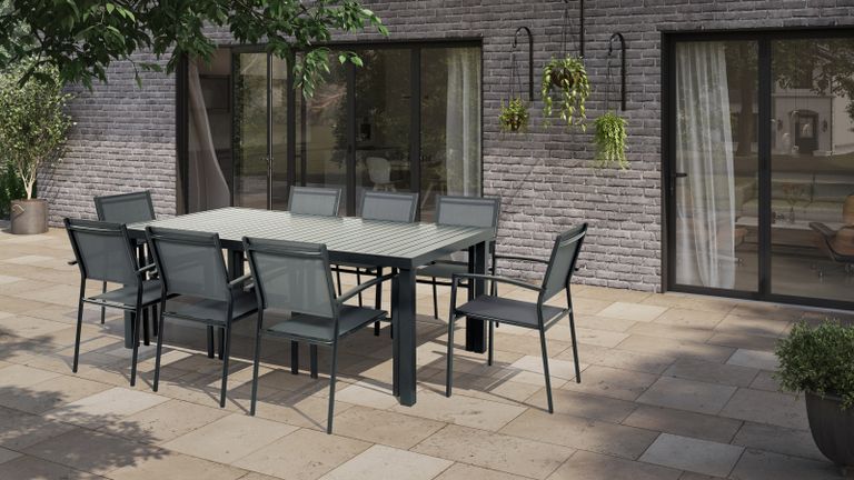 A grey-slabbed external patio floor tiles with grey dining set made up of eight chairs and large table in backyard with hanging plants and bi-fold sliding doors 