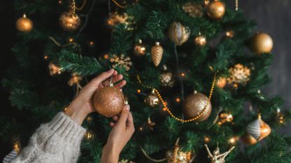 Close up image of woman's hand in sweater decorating christmas tree with bubblers. Womans hand in stylish sweater decorating christmas tree close up. Merry christmas and happy New Year concept. Space for text.