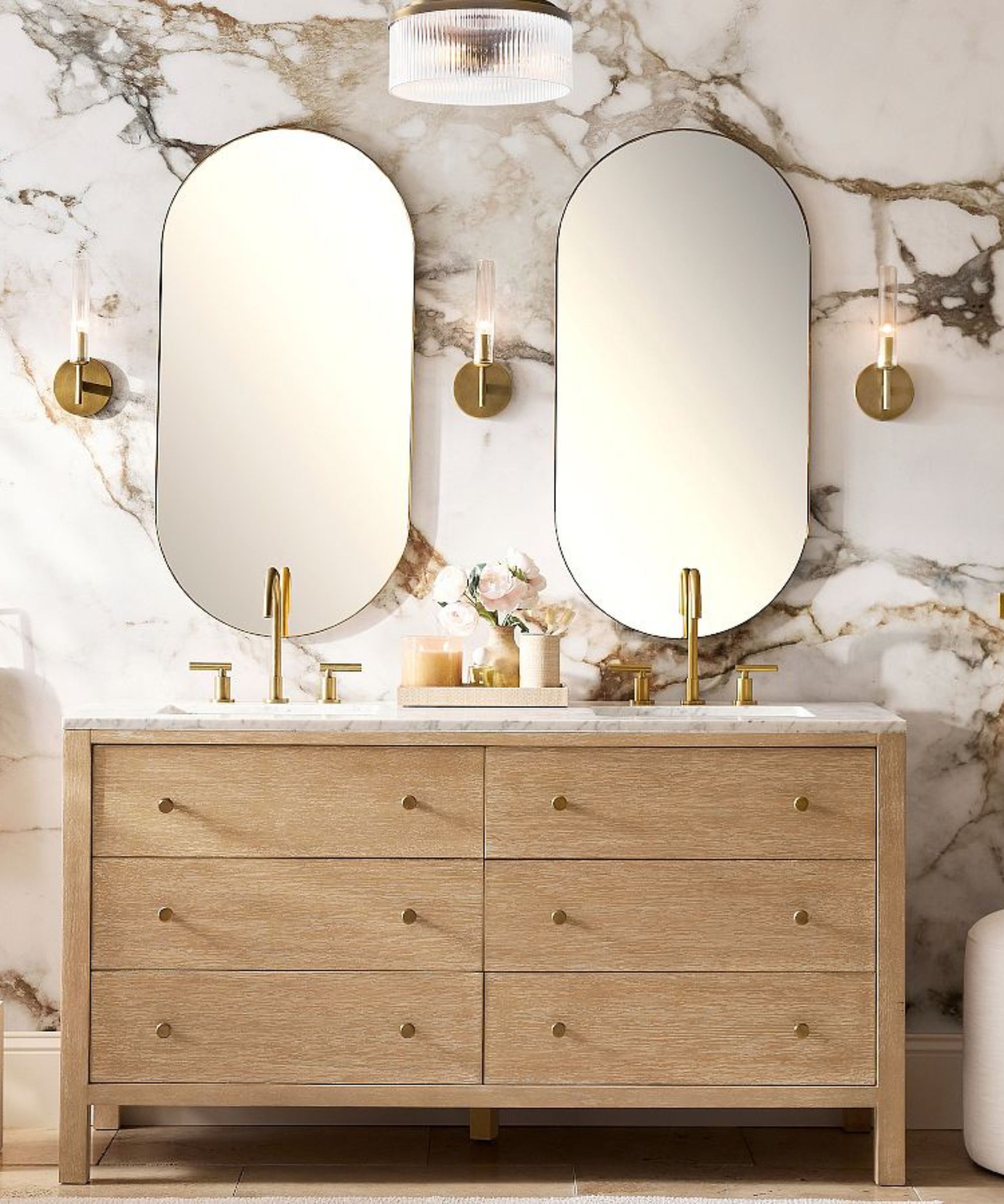A wooden double vanity with two gold framed pill-shaped mirrors above