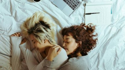 A couple cuddling each other while on a mattress, surrounded by notepads and a laptop