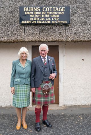 Prince Charles and Duchess Camilla stand together outside the home of poet Robert Burns, both dressed in tartan.