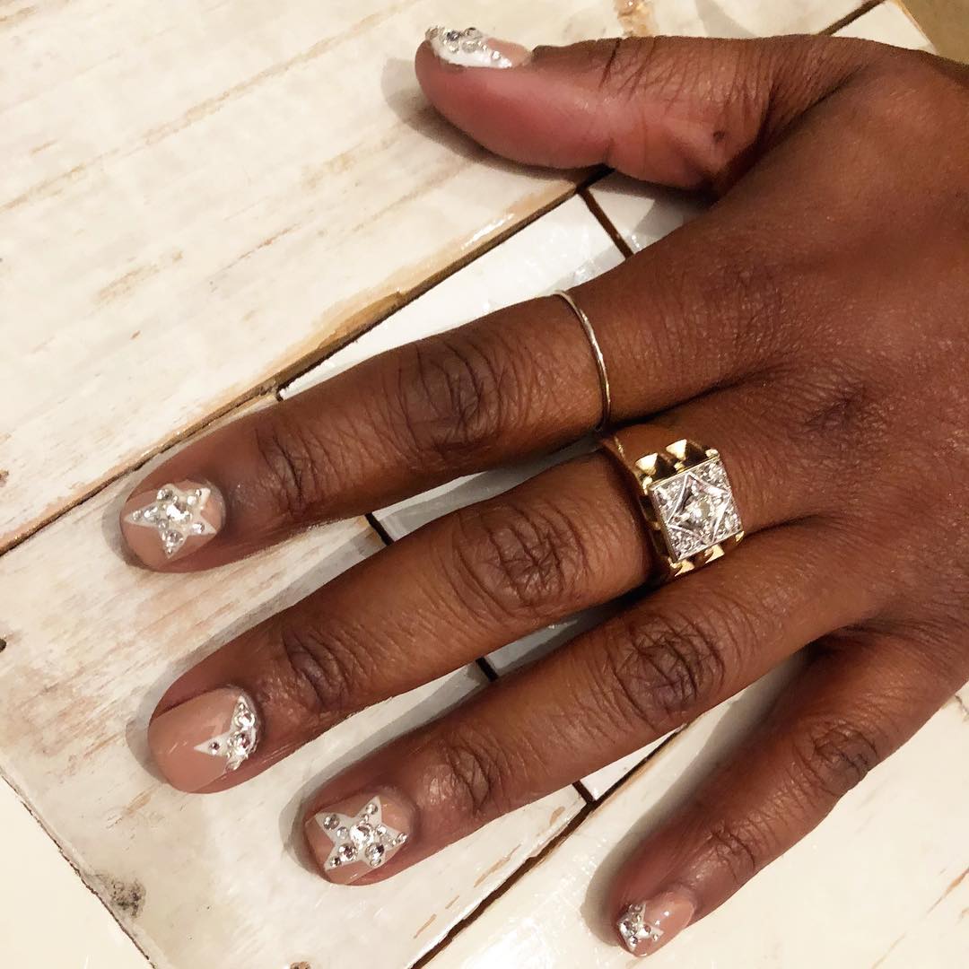 A hand with nude nail polish and bedazzled star detailing.