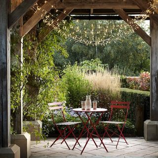 string lights overhead in a small courtyard area of an expansive garden, with a small red outdoor dining set