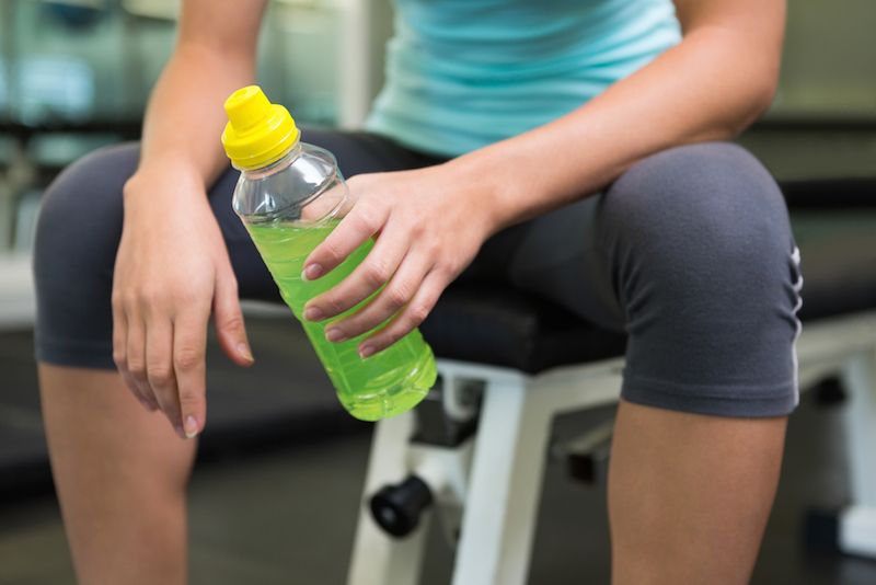 A woman holds an energy drink while working out at a gym.