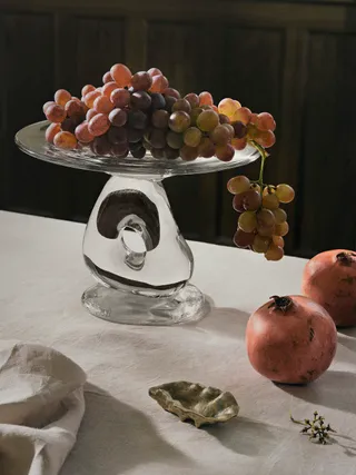 Some grapes and pomegranate lie on a table covered in a white table cloth.