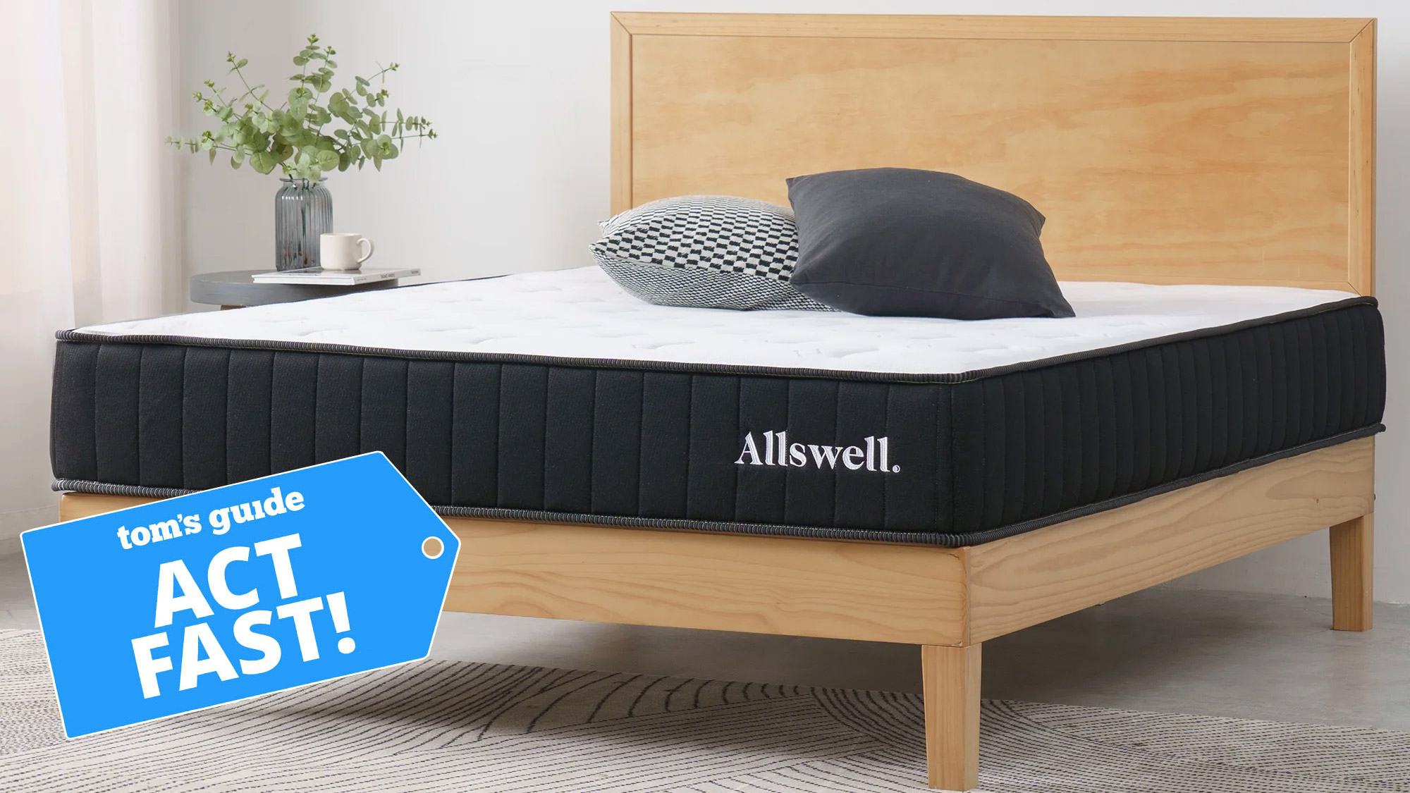 An Allswell mattress on a wooden bed in a light grey bedroom, with a blue Tom&#039;s Guide tag overlaid saying &quot;ACT FAST!&quot;