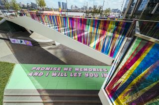 A floor painting with the words "Promise me memories and I will let you in" in pink type over a green background, created by Yinka Ilori for Greenwich Peninsula
