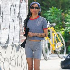 Zoe wears a bandana, gray t-shirt, and gray bike shorts with red sandals.