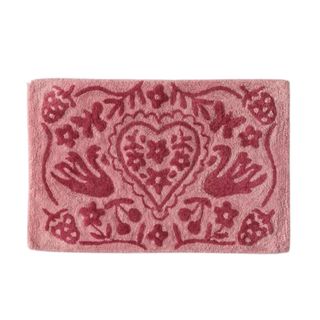 A rectangular dusky pink bath mat with a dark pink pattern with leaves, birds, and hearts on it