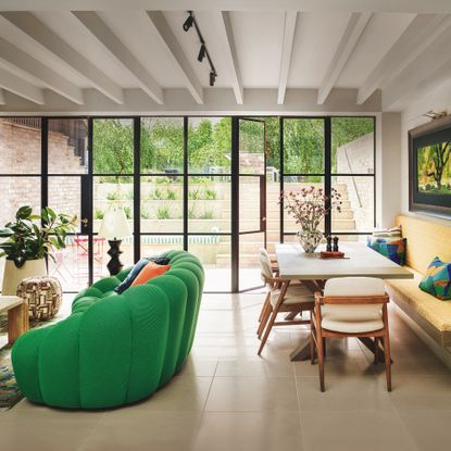 open plan kitchen living space with green sofa and wooden dining table with crittall sytle doors to courtyard garden