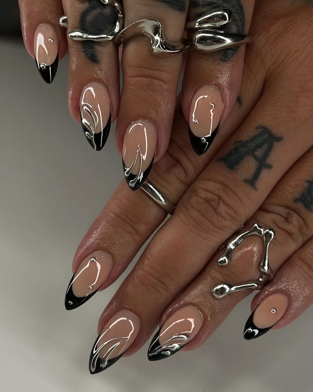 a close up photo of a person wearing a black French manicure with silver chrome designs
