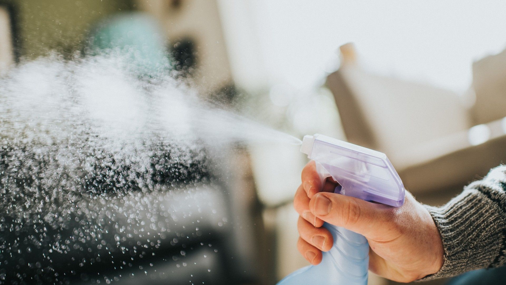 person cleaning a mirror with a spray cleaning product