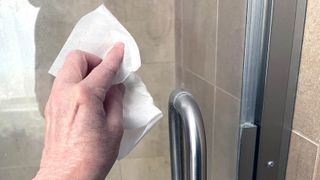 Someone cleaning a glass shower door with a dryer sheet