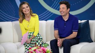 Jimmy Fallon promotes Wordle with Savannah Guthrie while sitting on the white couch on Today. She has a yellow top on and he is wearing a navy polo,