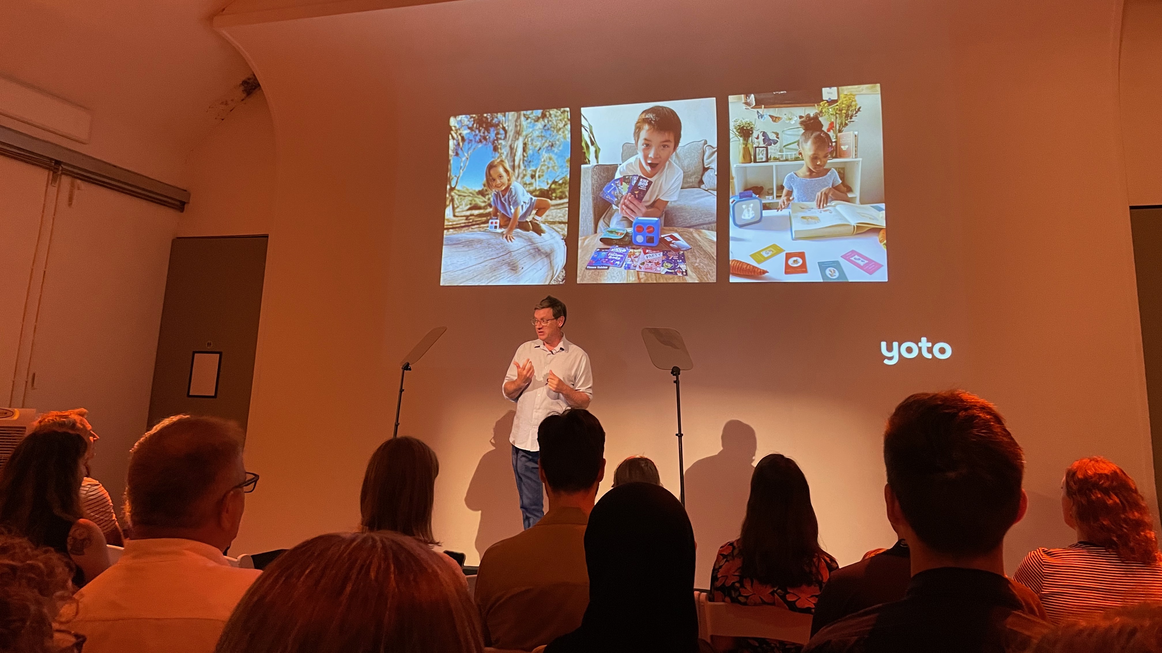 Ben Drury, CEO and co-founder of Yoto, giving a presentation on stage in front of photos of kids and their Yoto players.