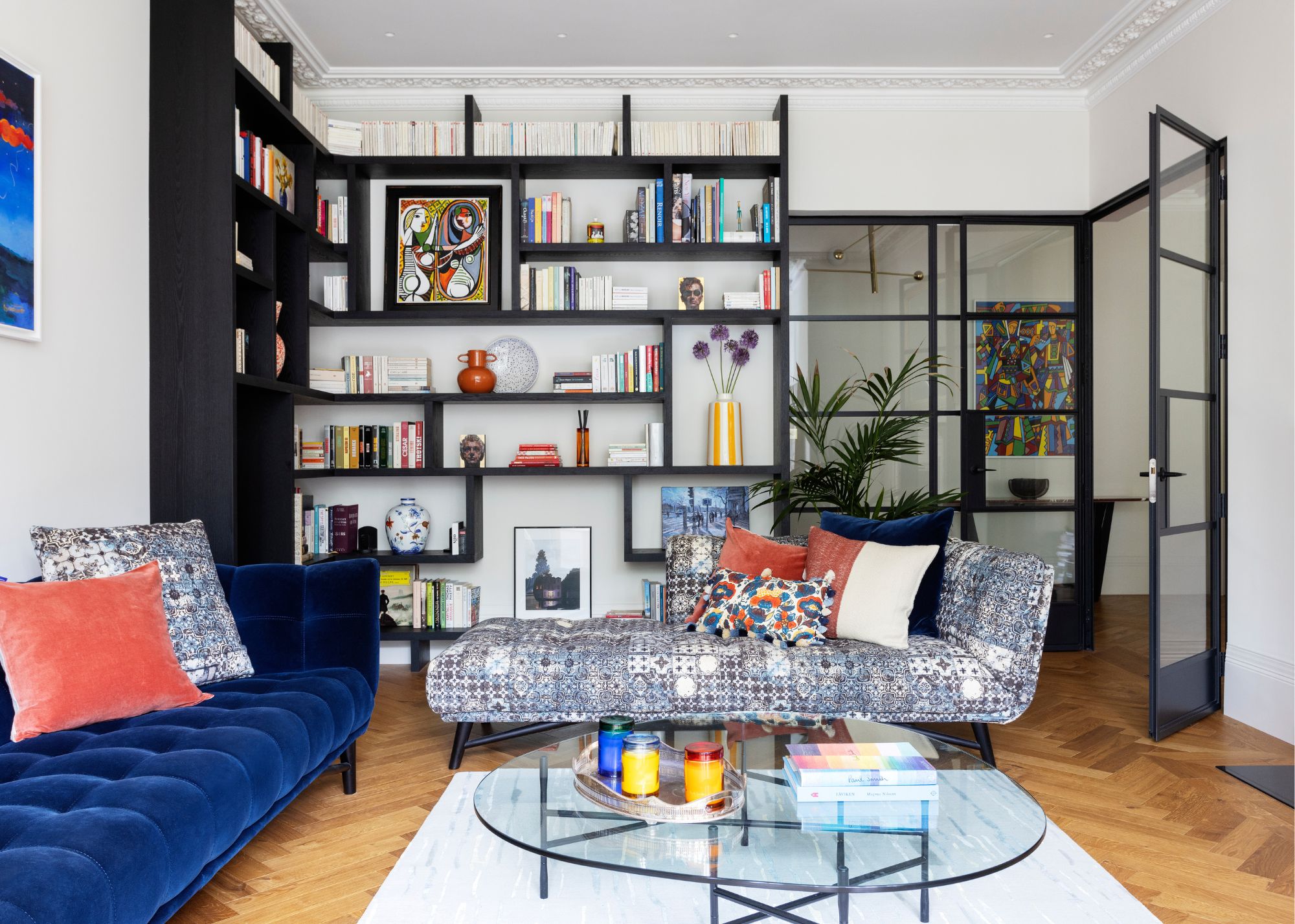 A living room with parquet wood floors, white walls, and black built-in shelving with books and decorative objects.