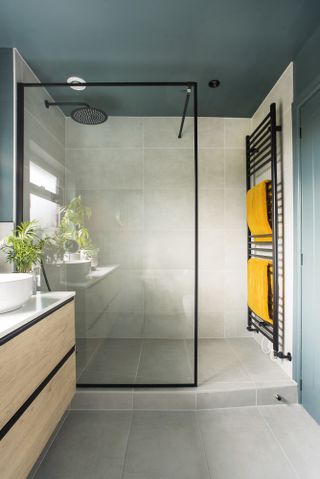 Bathroom with grey wall and floor tiles, blue painted ceiling, walk-in shower with black framed screen and black radiator