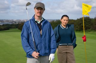 Barry Ward and Thaddea Graham, holding clubs and standing on a golf course, in "Bad Sisters."