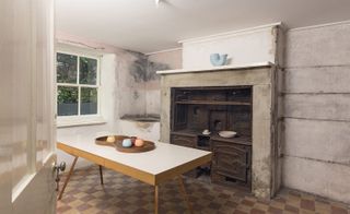 Olden day kitchen with coal stove, brown checkered floor tiles and wooden table.