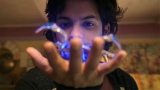 Still from the movie Blue Beetle (2023). Jamie Reyes (older teen, with short, dark curly hair) holding glowing blue scarab.