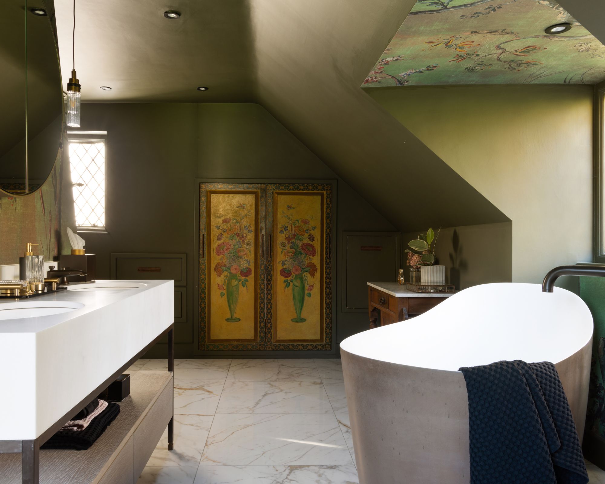 A bathroom with a freestanding bath and large his and her bathroom sinks. In the background are small cupboard doors painted with an intricate floral design