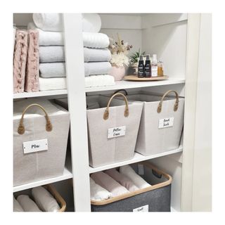 Organized linen cupboard interior in chic neutrals, with labelled baskets of different linen categories.