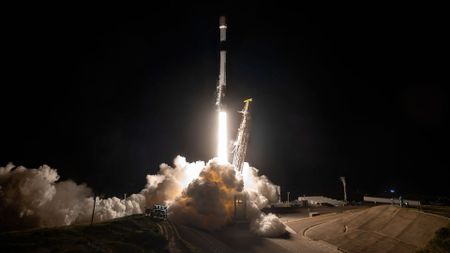 a rocket lifts off into the night sky, lighting up the area around its launch pad