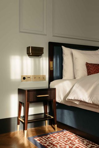Bedroom with wooden pedestal, brass wall lamp and herringbone marble flooring
