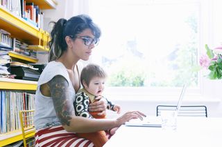mum with tattoos holding baby while looking at laptop