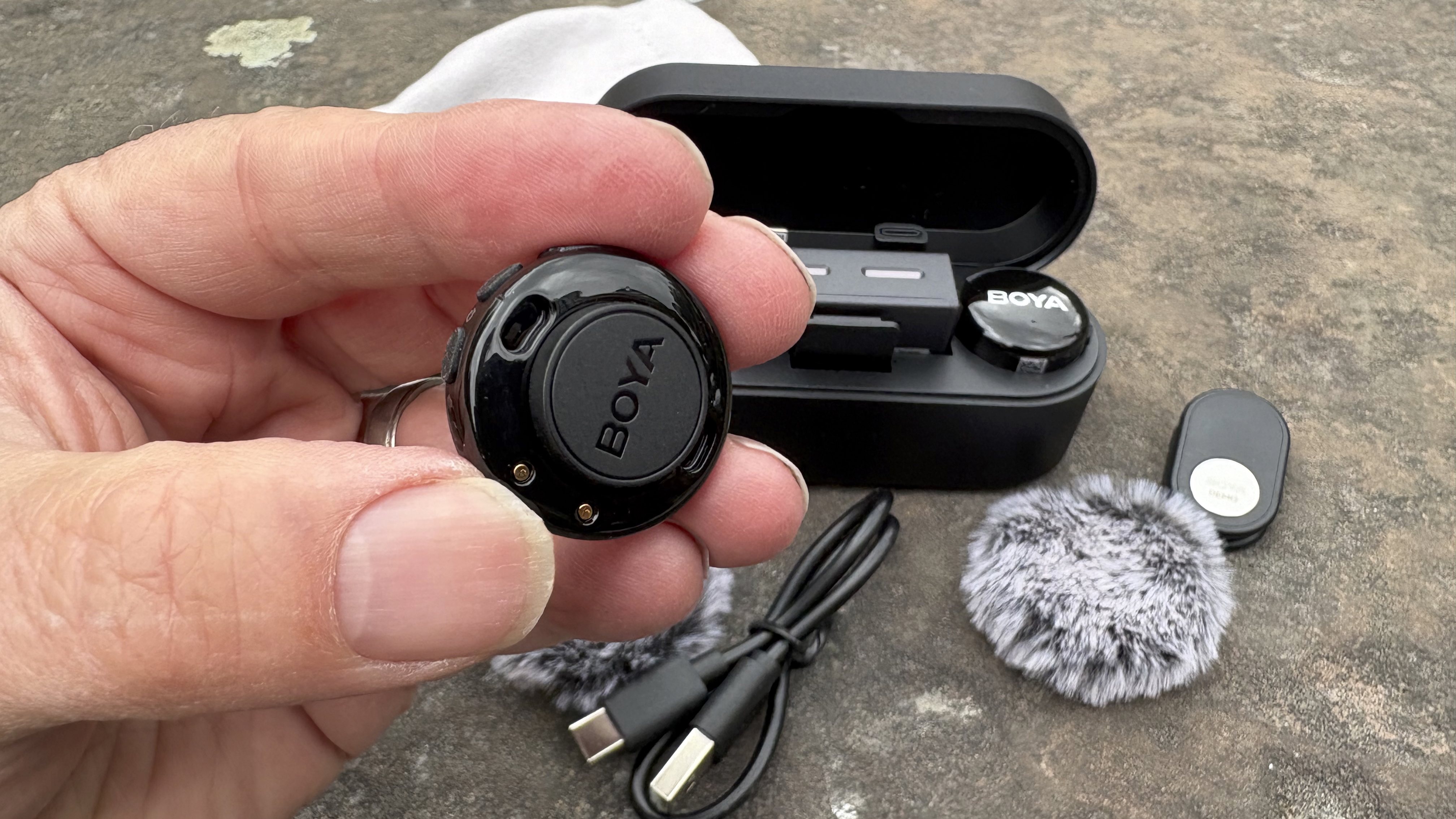 Close-up of a hand holding the disc-shaped Boya-branded 3 mic up to the camera to display the attached Boya-branded magnet