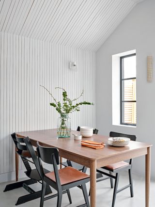 Wooden dining table and black chairs against white slatted panel wall
