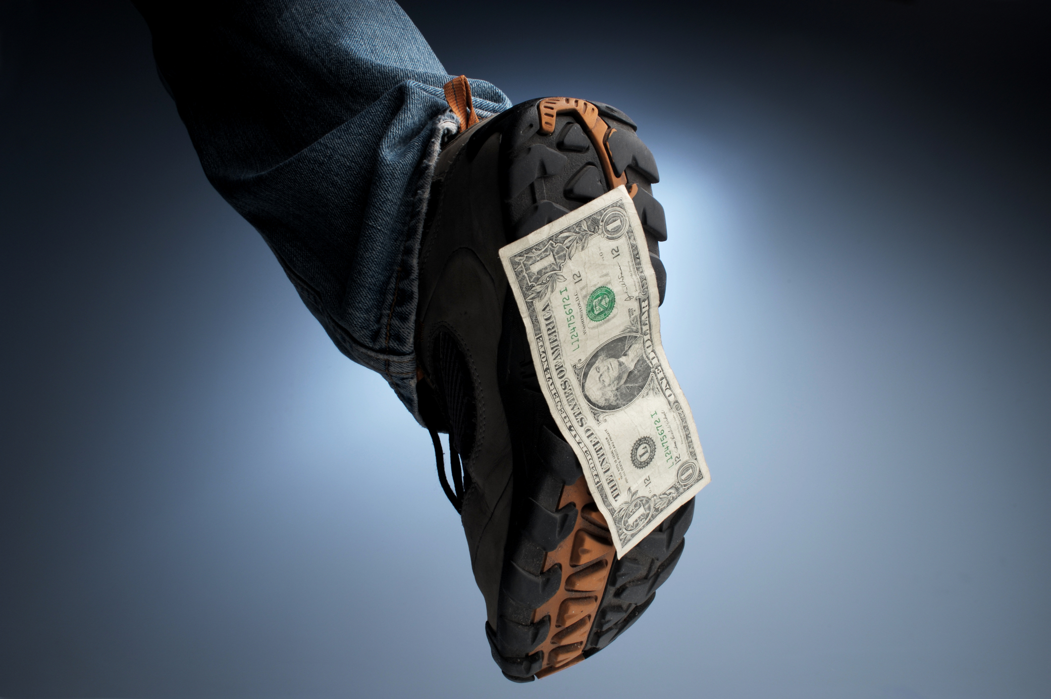 An outdoor boot or shoe with a dollar bill stuck to the bottom of it