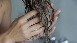 A women's hand rubbing a hair treatment into her wet hair