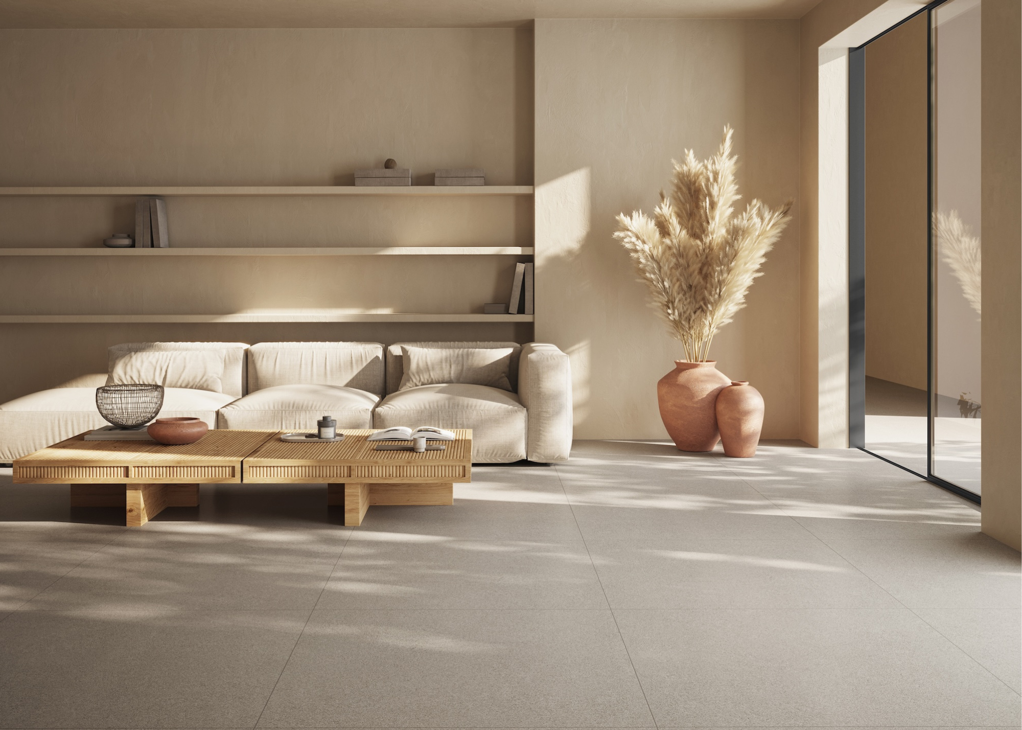 A living room with a neutral color scheme, large format floor tiles, and a low cream sofa and coffee table with open shelving behind and patio doors half open at the side next to a large pot filled with pampas grass