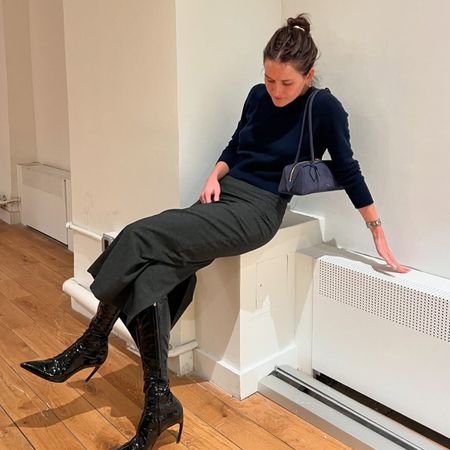 Eliza Huber wearing a navy blue sweater and handbag with a charcoal gray pencil skirt and black boots..