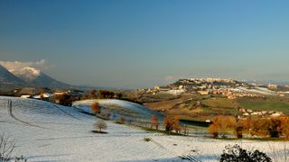 Photo of the town of Camerino in Italy's Apennine Mountains with snow on the hillside and the town in the green valley below.