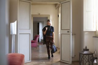 Woman walking out of bedroom smiling with leopard print trousers and bag