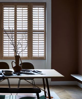 dining room with natural wood shutters, chocolate walls, wood desk, vases, table runner,