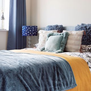 Guest bedroom with white walls, blue curtains, textured cushions, blue throw and animal print table lamp
