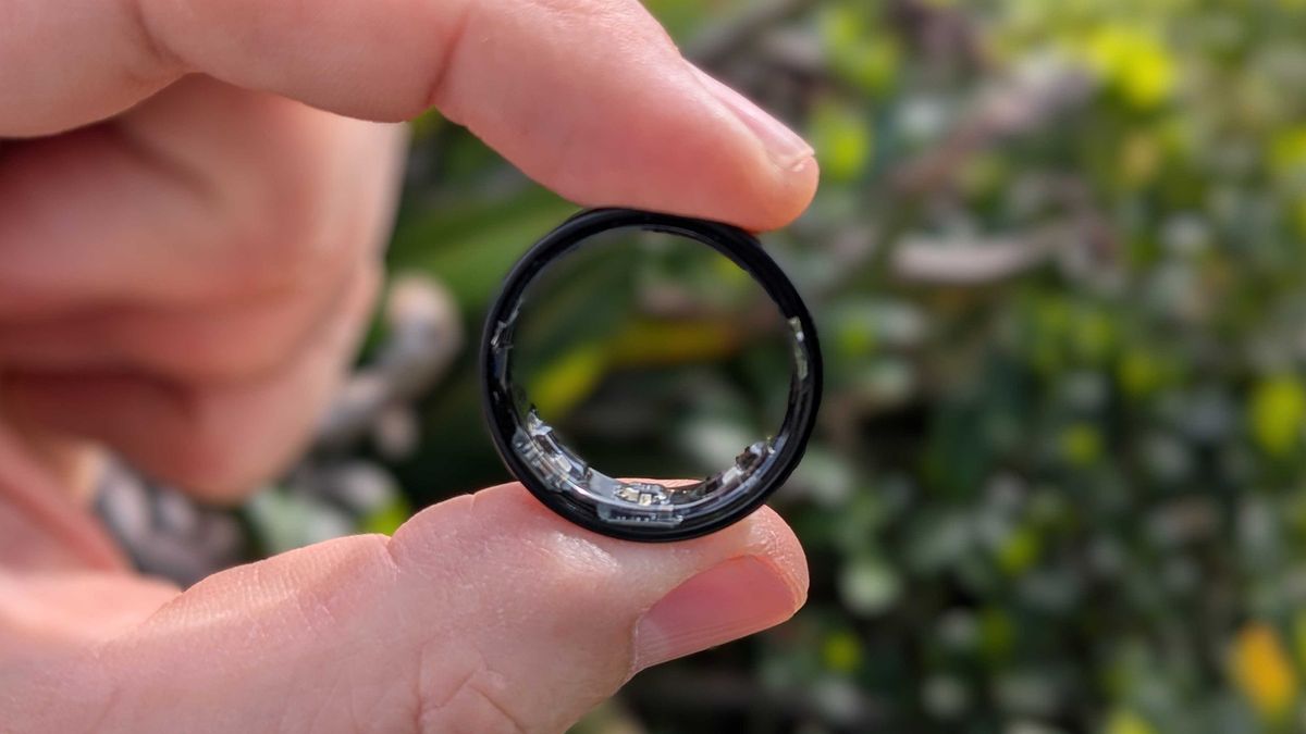 Samsung Galaxy Ring held between index finger and thumb in front of a garden area.