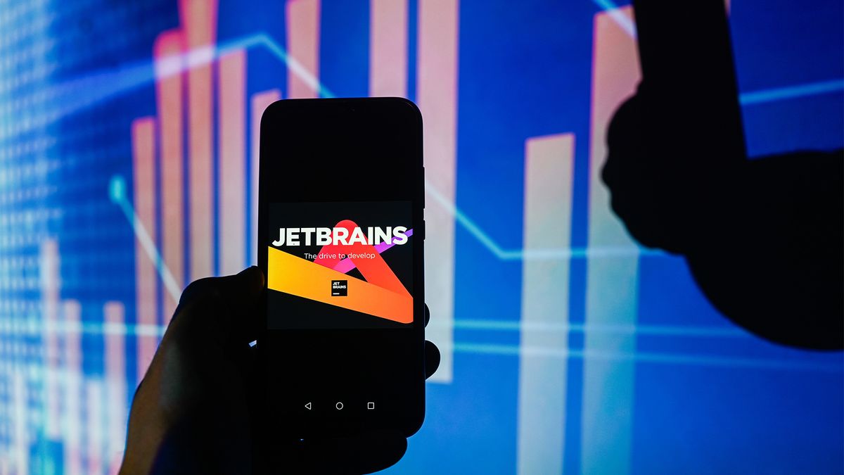 JetBrains logo and branding pictured on a smartphone held up in front of stock market chart.