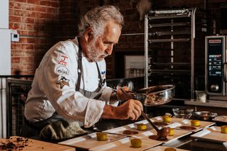 Chef Janos Wilder ladles sauce over food on white plates