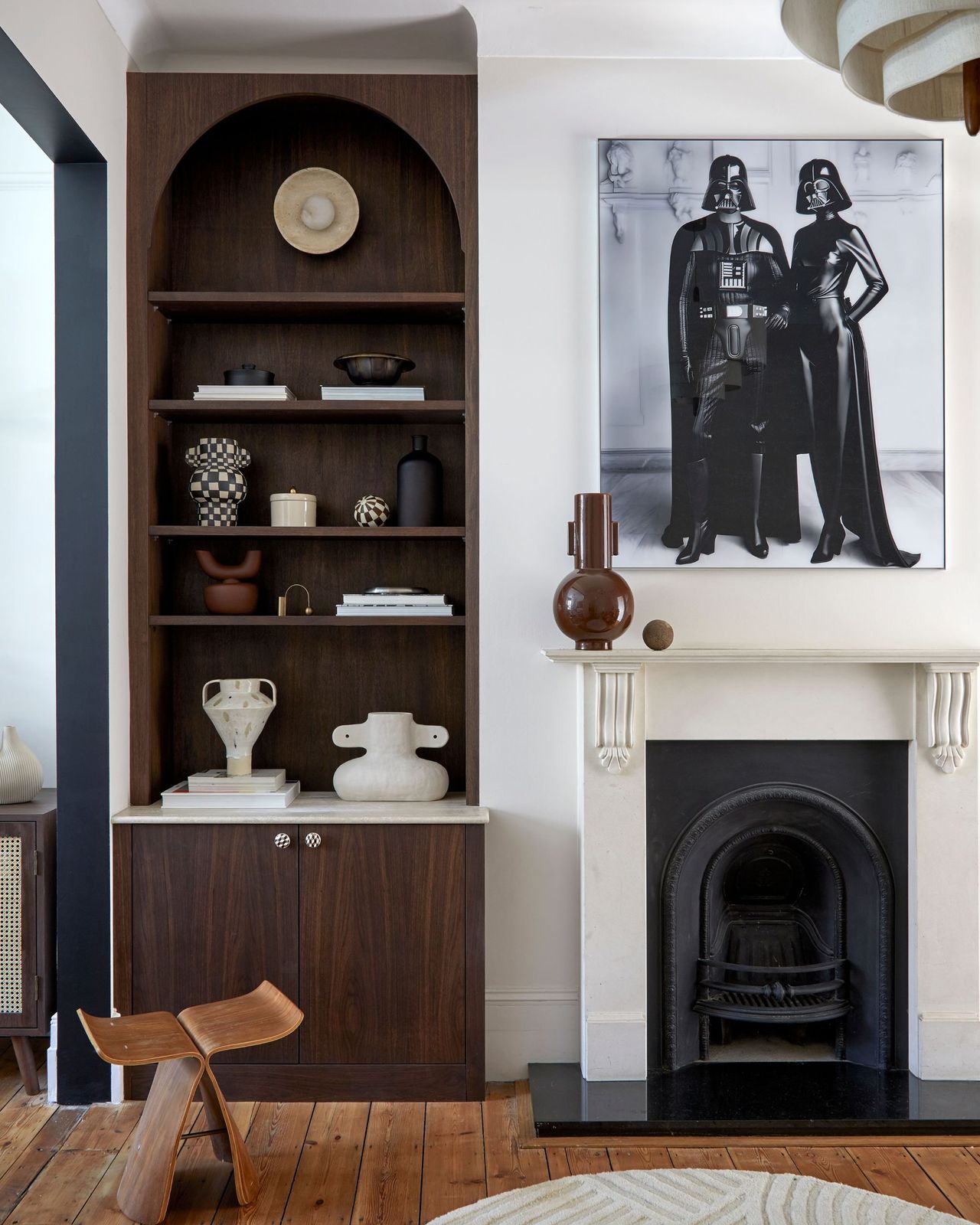 A modern living room with an arched dark wood alcove shelving unit next to a fireplace with a star wars-esque black and white print above it