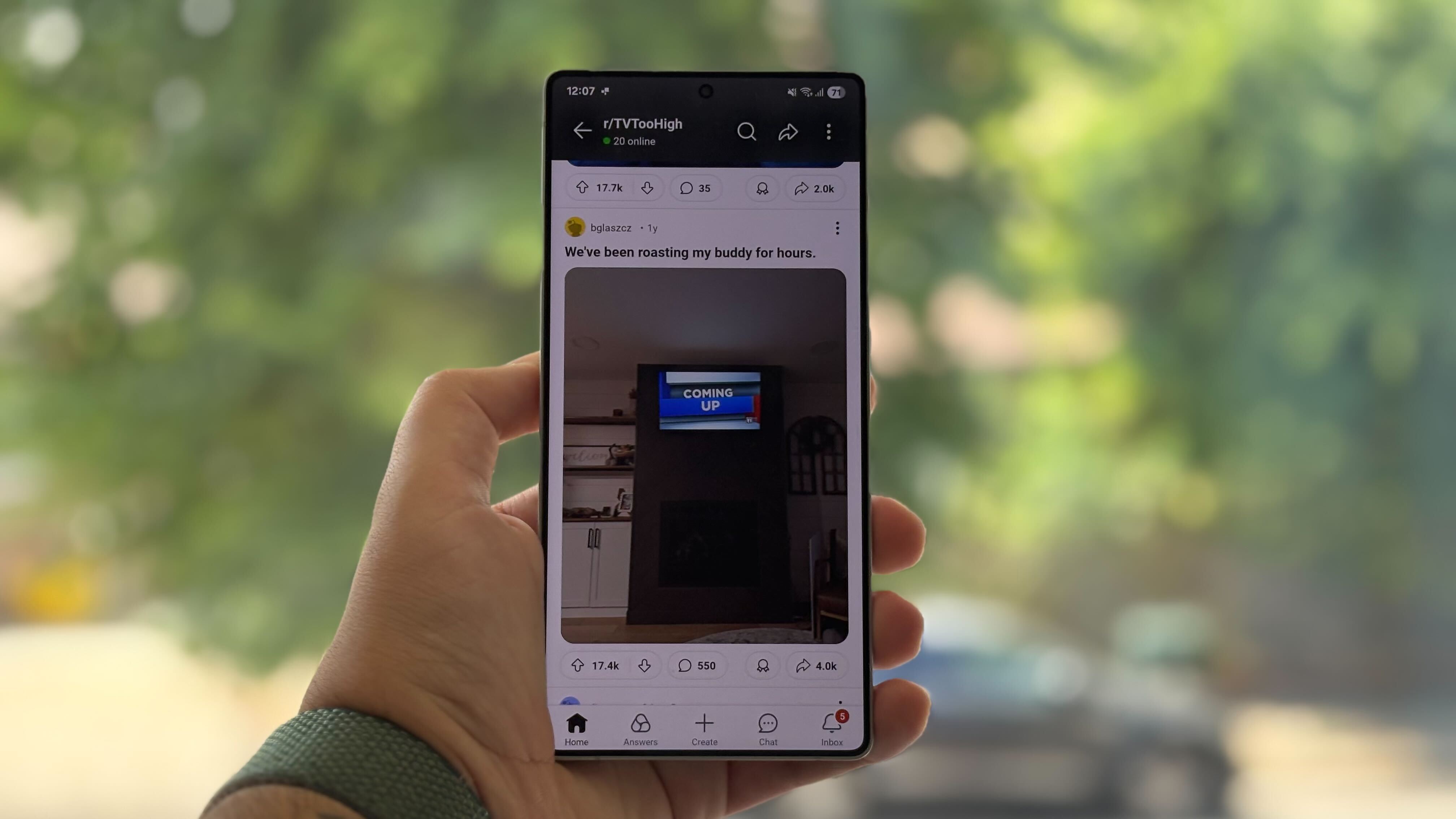A hand holding a phone with the Reddit forum TV Too High On Screen