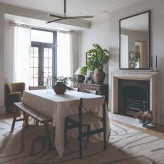 A dining area in an open-plan space with a rectangular dining table covered with a white tablecloth placed in front of a fireplace