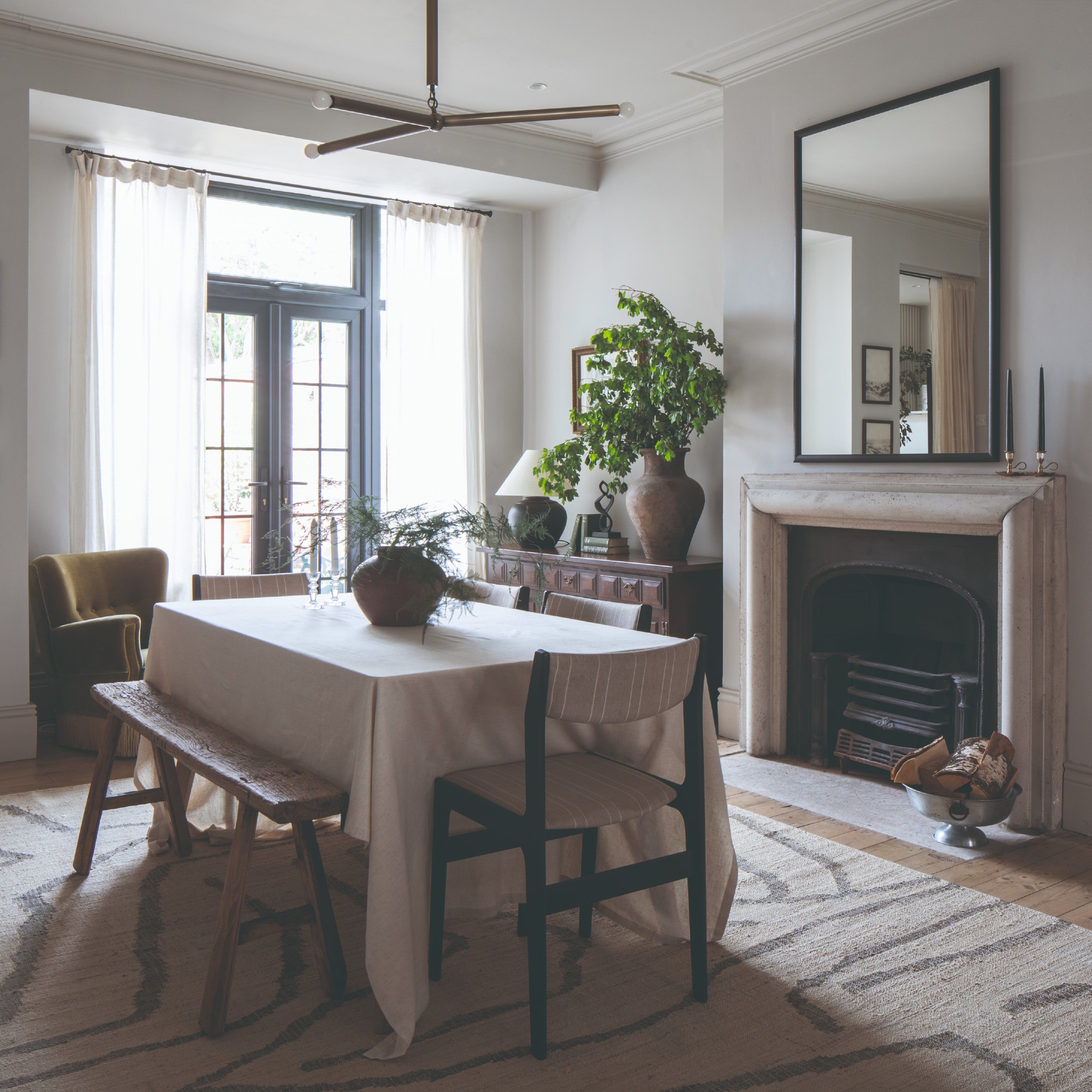 A dining area in an open-plan space with a rectangular dining table covered with a white tablecloth placed in front of a fireplace