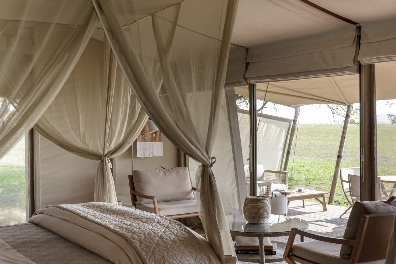 The inside of a luxurious safari tent featuring a four poster bed with sheer linen drapes