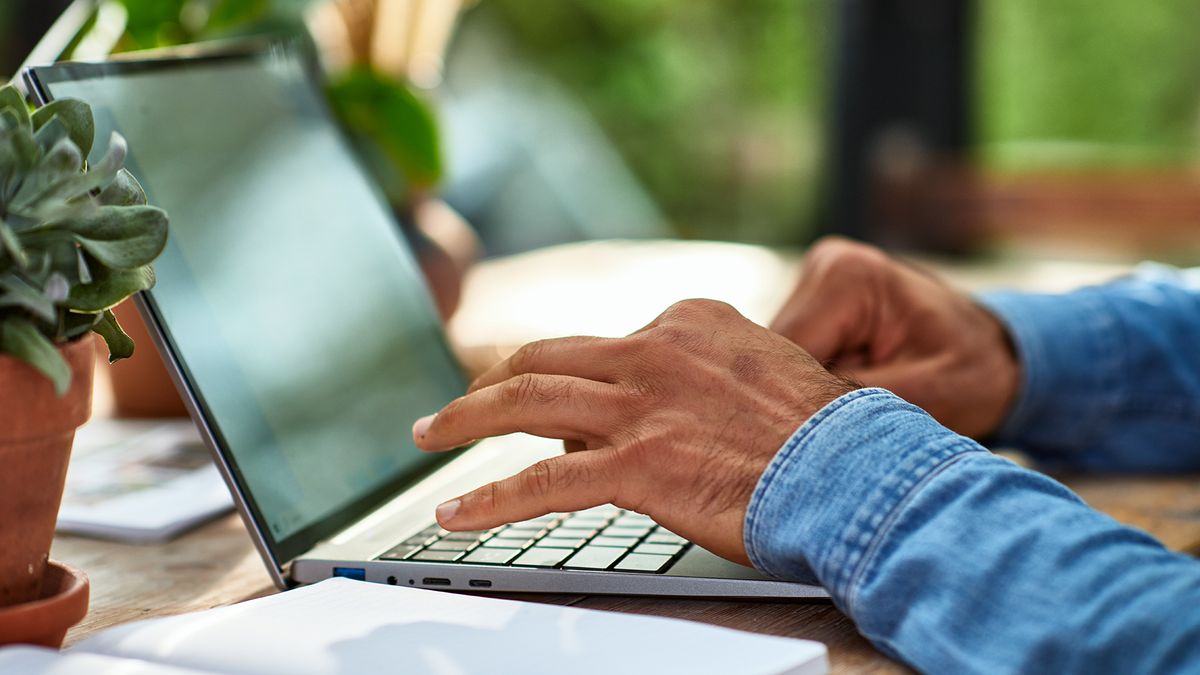 Man typing on a laptop on a table.