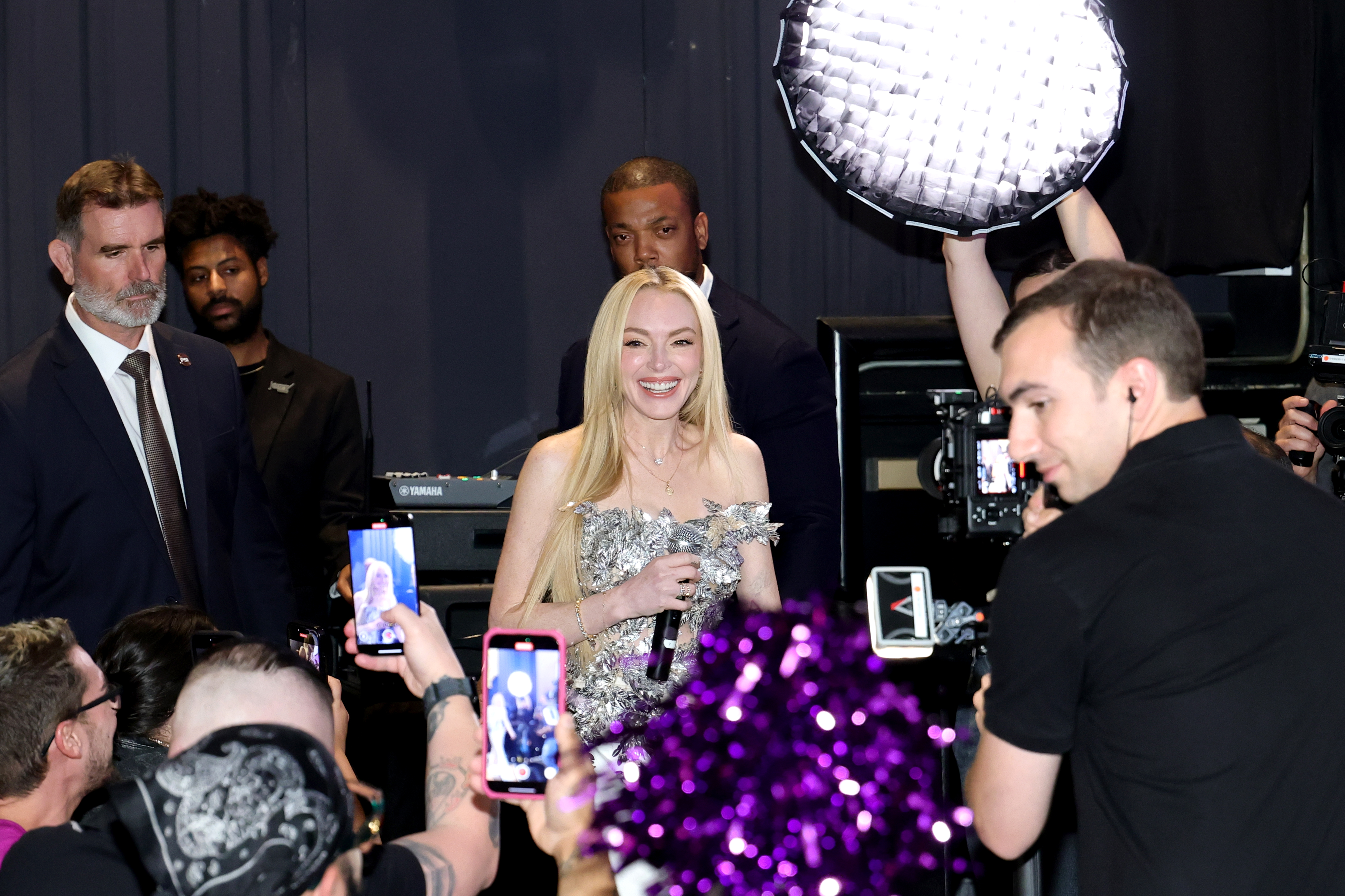 Lindsay Lohan wears a metallic strapless top, white pants, a Cartier watch, and carries an Hermes Kelly bag