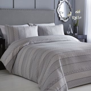 bedroom with grey wall white tile flooring mirror on wall and grey striped blanket and pillow